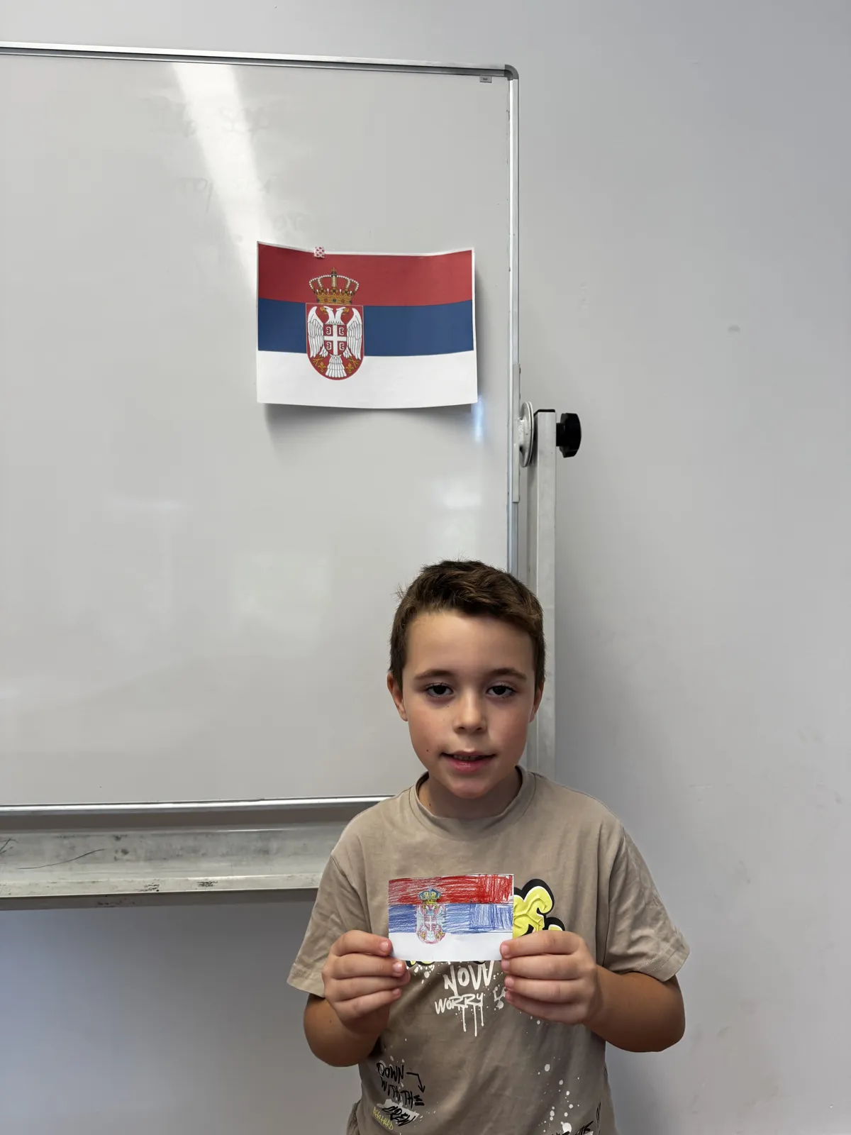 Ученик са обојеном заставом испред заставе Србије